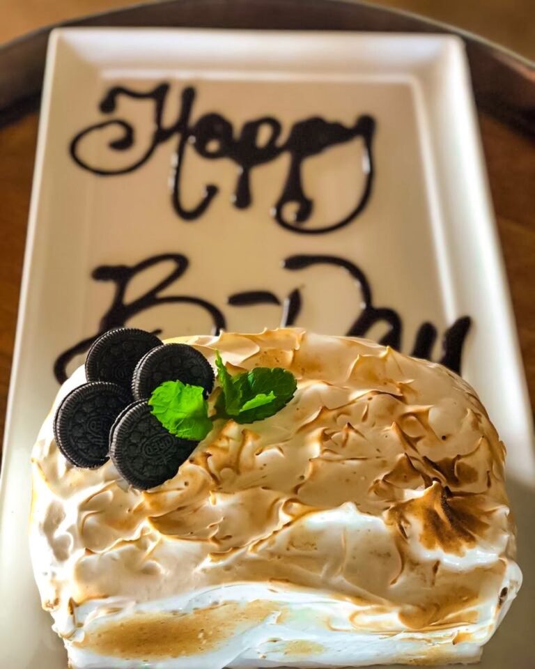 Birthday cake topped with meringue and cookies beside a Happy Birthday plate