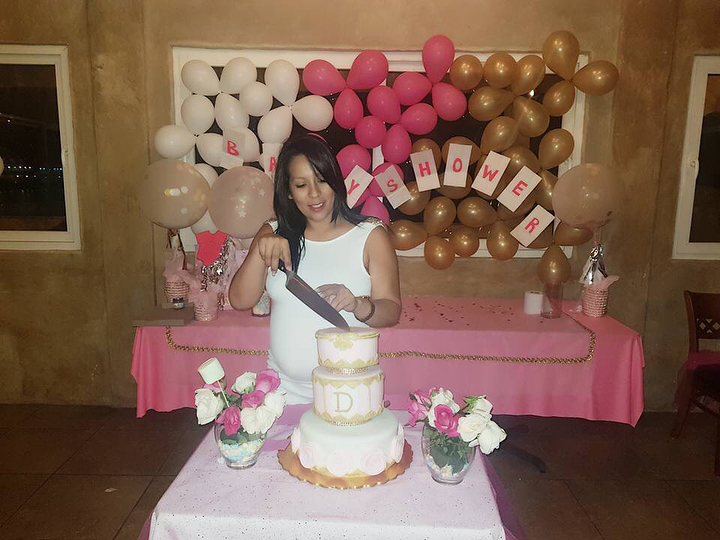 Guest cutting the cake at a baby shower with balloons and a decorated table