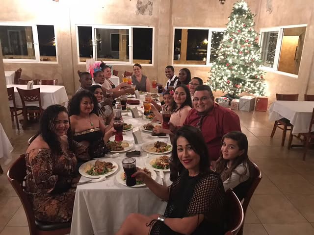 Large group raising their glasses at a dinner, with a Christmas tree behind them