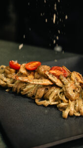 Linguini with shrimp and cherry tomatoes being finished with grated cheese