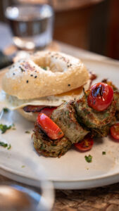 Bagel sandwich with egg and bacon, served with courgette fritters and tomatoes