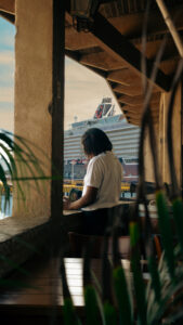Guest seated by the window with a cruise ship docked across the water