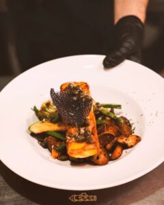 Chef plating a grilled fillet with capers, green beans and roasted potatoes