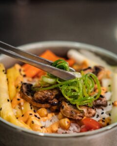 Rice bowl with mushrooms, pineapple, carrot and spring onion, served with tongs