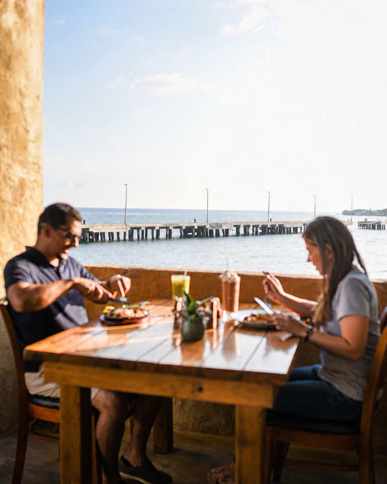 Couple having lunch by the window with the pier and the sea behind them