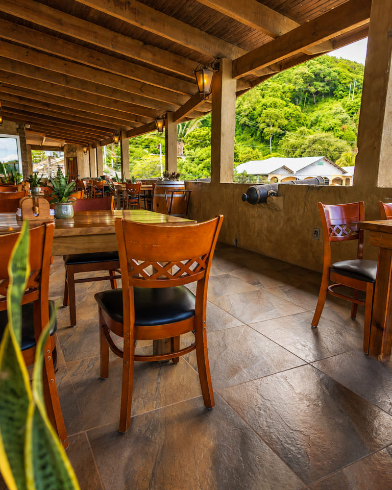 Covered terrace with wooden tables, a cannon and a view of the green hillside