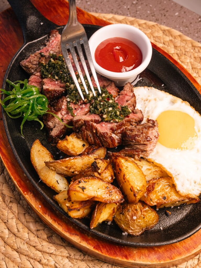 Steak with chimichurri, fried egg and roasted potatoes in a skillet